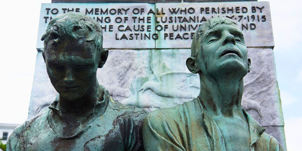 Bronze statue of two anguished men in front of a memorial plaque commemorating victims of the Lusitania sinking in 1915.