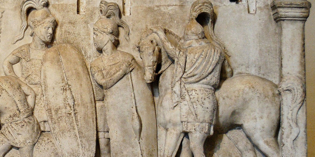 Ancient stone relief showing Roman soldiers in armor with shields and a horse, carved into a wall with architectural details.