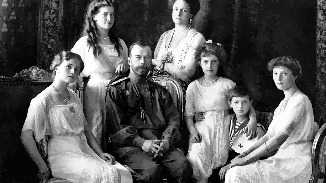 A historical black-and-white portrait of a royal family, with a bearded man in military attire seated at the center, surrounded by elegantly dressed women and a young boy in a sailor suit.