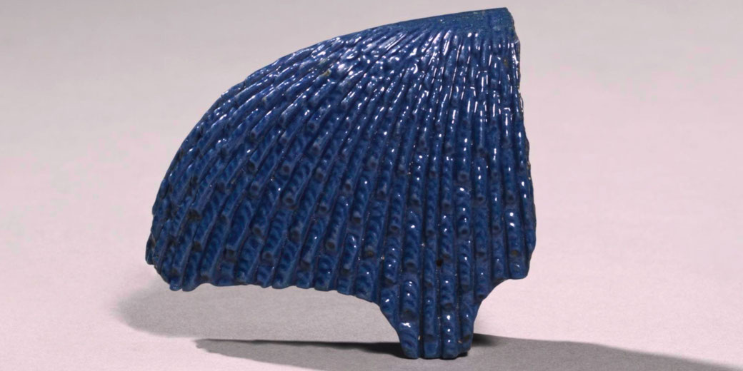 Blue faience fragment from a queen's headdress, featuring curled design and ear tab, likely part of an inlaid figure.