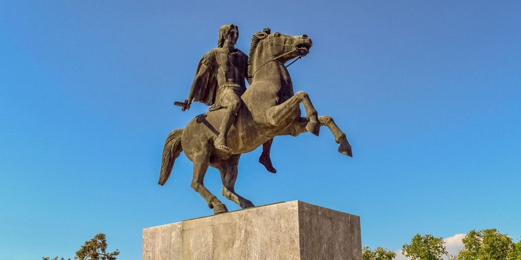 Bronze equestrian statue of a warrior holding a sword atop a stone pedestal against a clear blue sky.