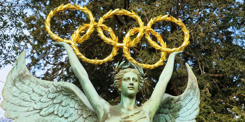A statue of a winged victory holding golden Olympic rings, located at the Olympic Museum in Lausanne, Switzerland. It symbolizes the Olympic spirit and the pursuit of excellence in sports.