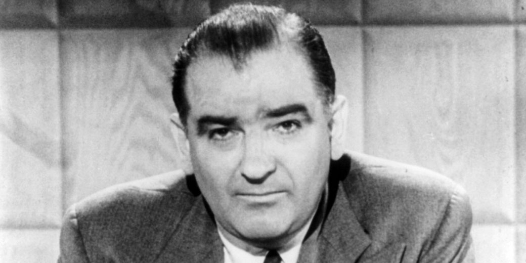 Black and white close-up portrait of a middle-aged man in a suit, looking directly at the camera with a serious expression. Soft focus background and classic mid-20th-century style.