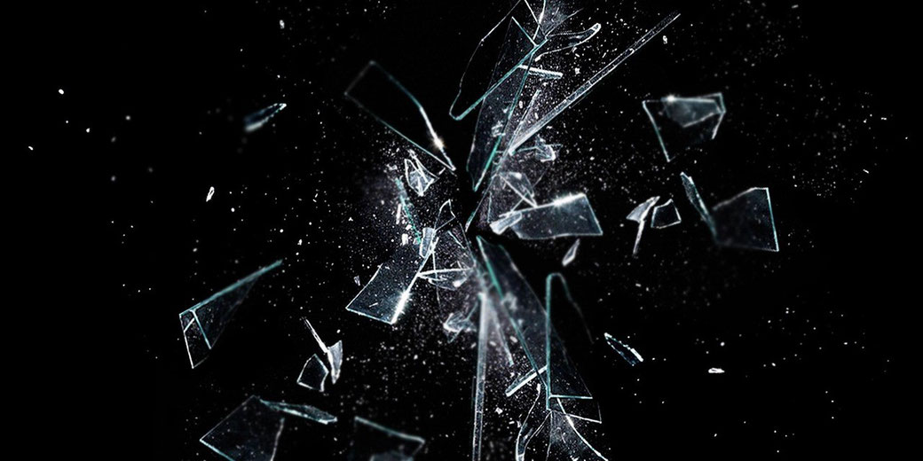 Glass shards exploding outward in midair against a black background, with fragments and particles captured in motion.