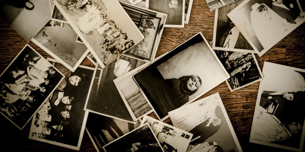 A scattered collection of vintage black and white photographs lies on a wooden surface, showing various people and moments from the past.