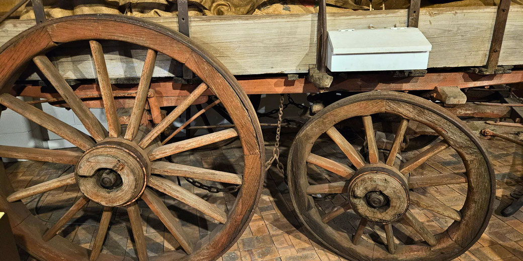 Close-up of a vintage wooden wagon with large spoked wheels and visible metal hardware, displayed on a brick floor.
