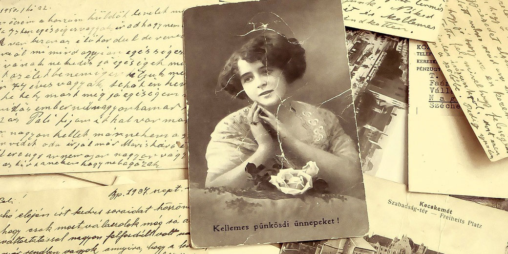 A vintage black-and-white postcard of a woman is placed atop handwritten letters in cursive script.