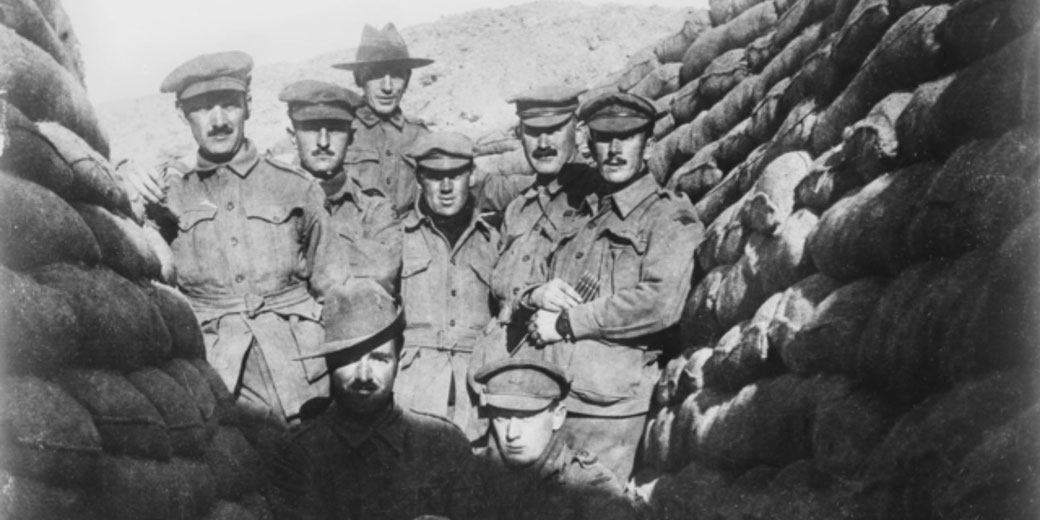 Black and white photo of uniformed soldiers standing in a narrow trench, posing together with serious expressions during wartime.