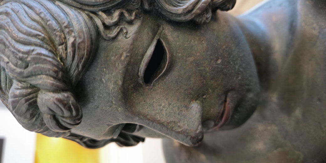 Close-up of a bronze statue’s face with hollow eyes, soft features, and wavy hair, showing detailed craftsmanship and a serene expression.