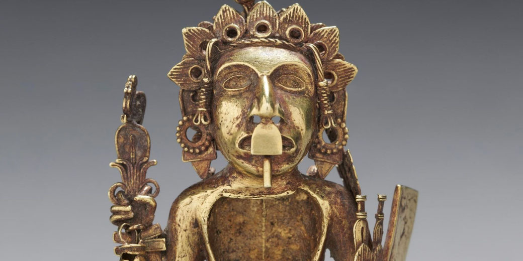 Small cast metal figure of an Aztec warrior holding darts and a shield, wearing jewelry and sandals, with an open chest cavity and glyphs on the back.