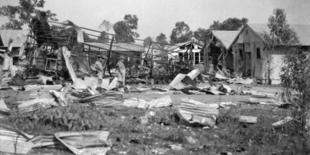 Twisted metal and debris cover the ground as soldiers inspect the wreckage of destroyed buildings after an air raid.