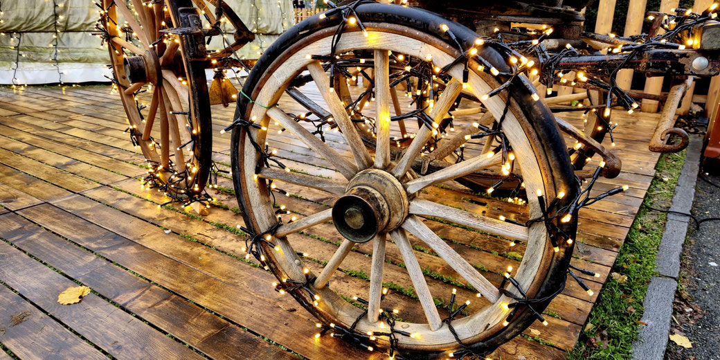 A rustic wooden wagon decorated with glowing string lights stands on a wooden platform, creating a festive and nostalgic atmosphere with its vintage wheels wrapped in warm illumination.