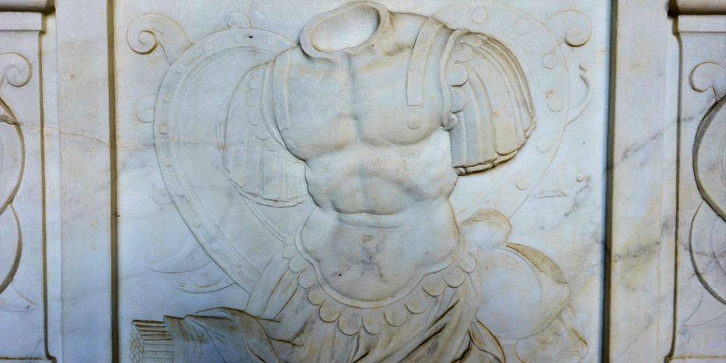 Marble relief of a muscular, headless torso in ornate armor, with a shield and drapery behind, symbolizing a fallen or idealized warrior.