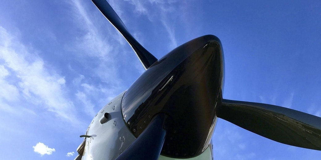 Low angle view of a propeller aircraft nose and blades against a sky with thin clouds, emphasizing aviation engineering, power, and mechanical flight technology.