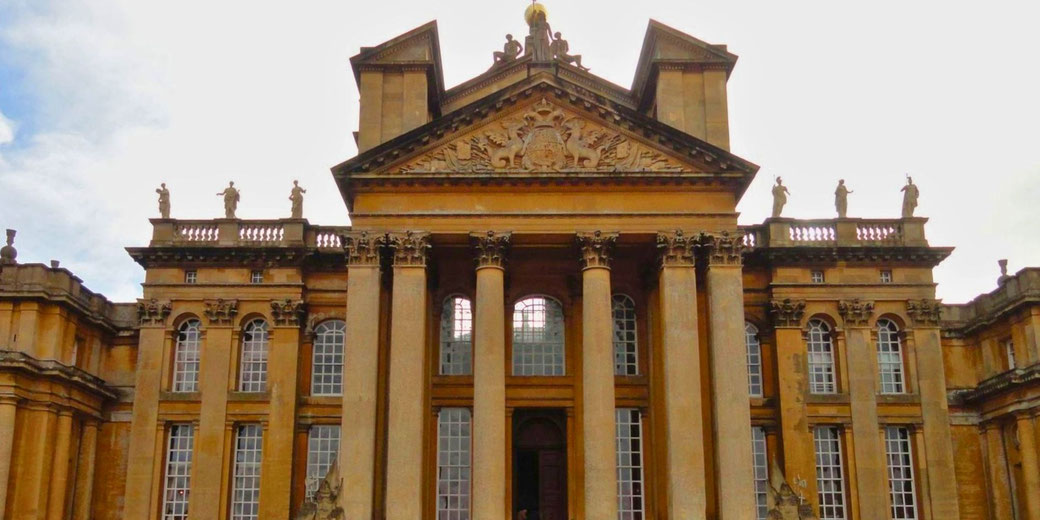Blenheim Palace, an English Baroque masterpiece with grand Corinthian columns, a decorated pediment, and statues adorning the roofline. The historic estate was the birthplace of Winston Churchill.