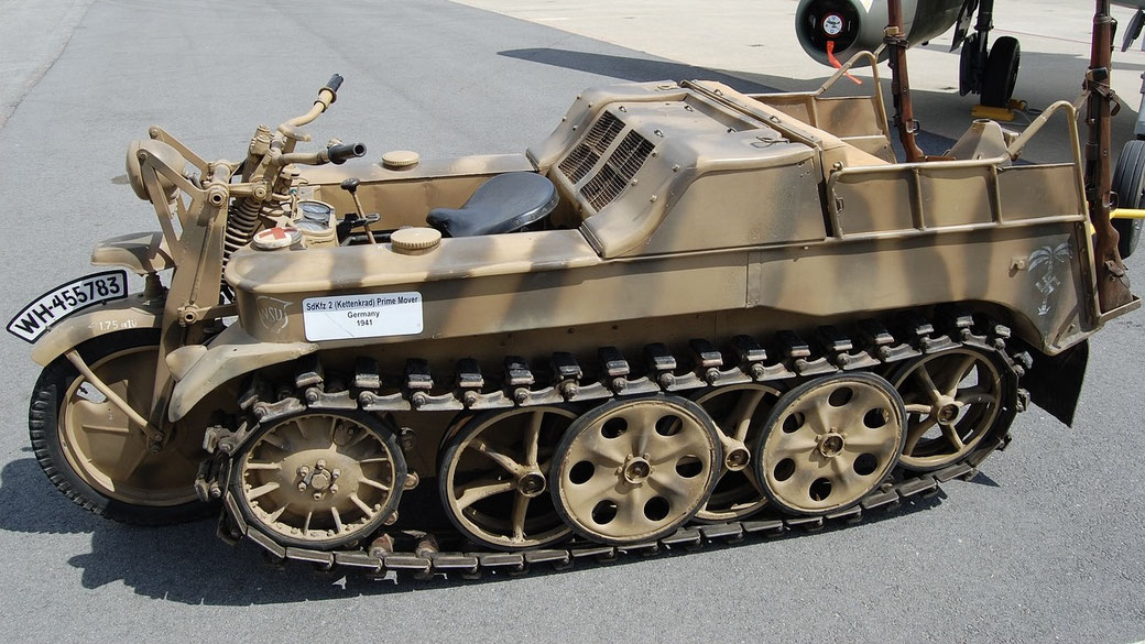 A vintage German SdKfz 2 Kettenkrad tracked motorcycle from 1941, painted in desert camouflage, is parked on a paved surface.