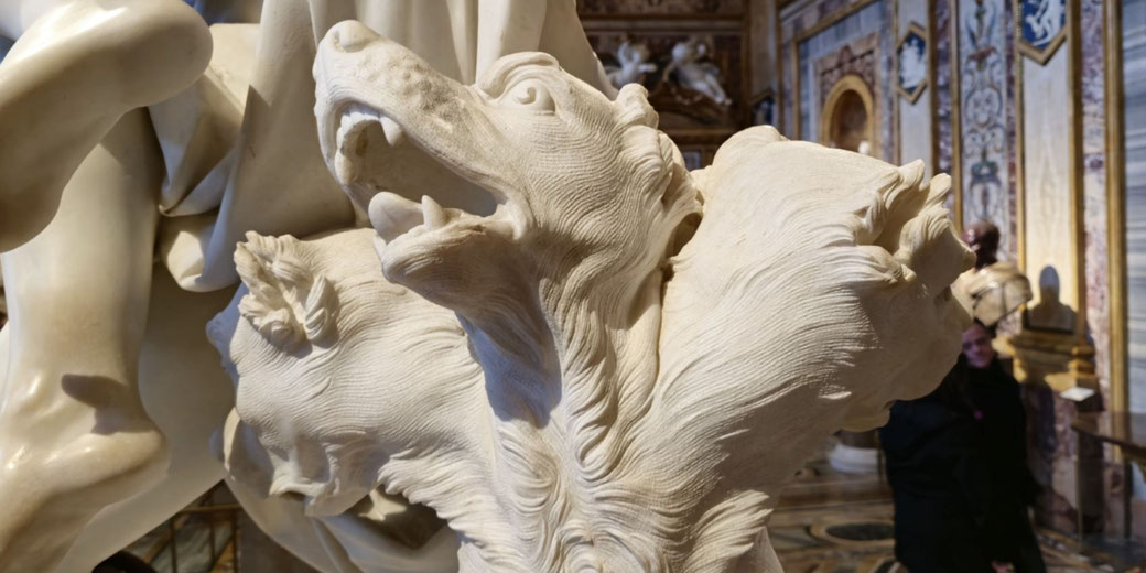 Marble sculpture of Cerberus, the three-headed dog, with snarling mouths and detailed fur, part of a mythological scene in an ornate gallery.