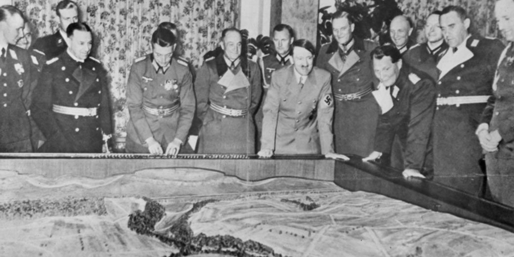 Nazi officials gather around a large topographical map during a World War II military planning session.