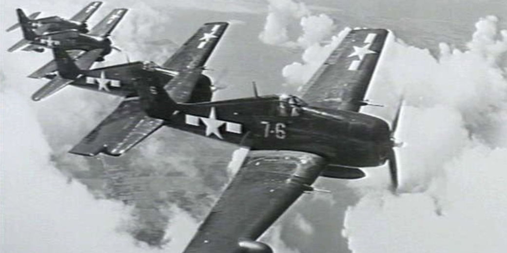 A formation of U.S. Navy fighter planes flies above the clouds during World War II, captured in a black-and-white photo.