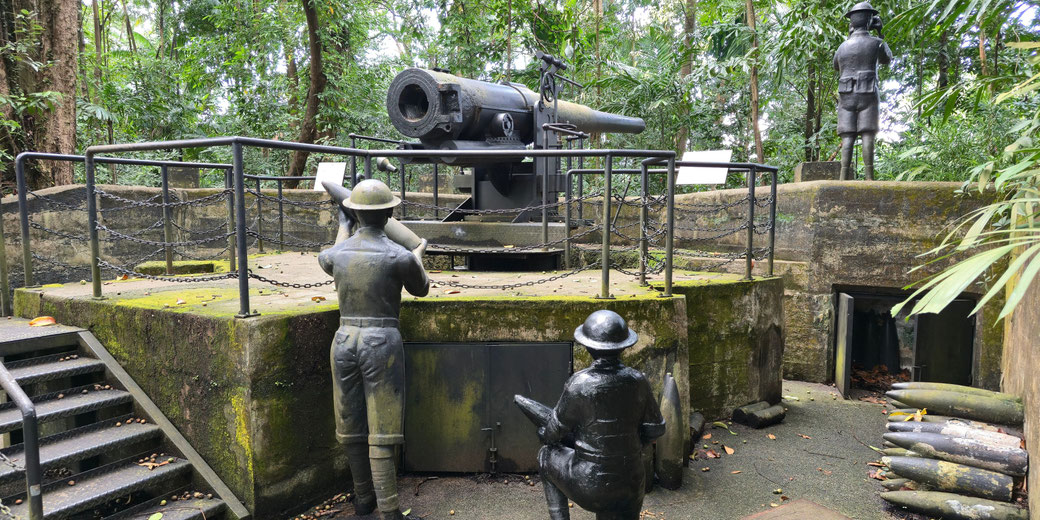 A coastal artillery gun with two soldier statues loading shells on a moss-covered concrete battery, framed by dense tropical forest and scattered ammunition rounds.