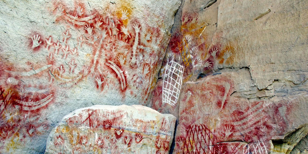 Ancient First Nations rock art with red ochre handprints and intricate patterns on a weathered rock face, reflecting early human expression and cultural heritage.
