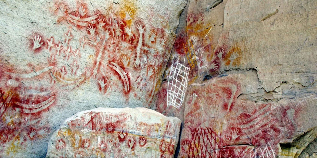 Ancient First Nations rock art with red ochre handprints and intricate patterns on a weathered rock face, reflecting early human expression and cultural heritage.