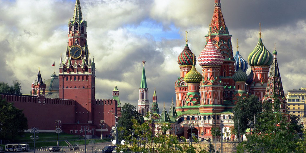 Colorful domes of Saint Basil's Cathedral beside the red walls and clock tower of the Kremlin under a cloudy sky.