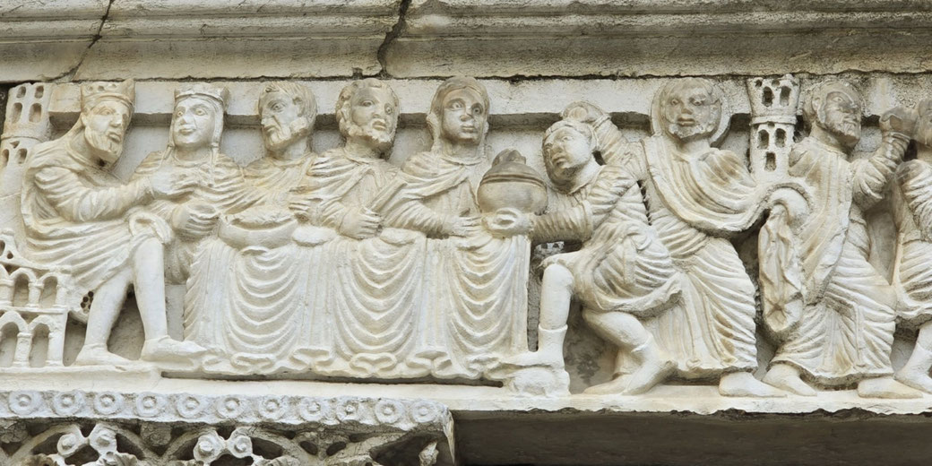 Stone relief carving above a doorway shows a biblical feast scene with multiple robed figures seated at tables, engaged in conversation.