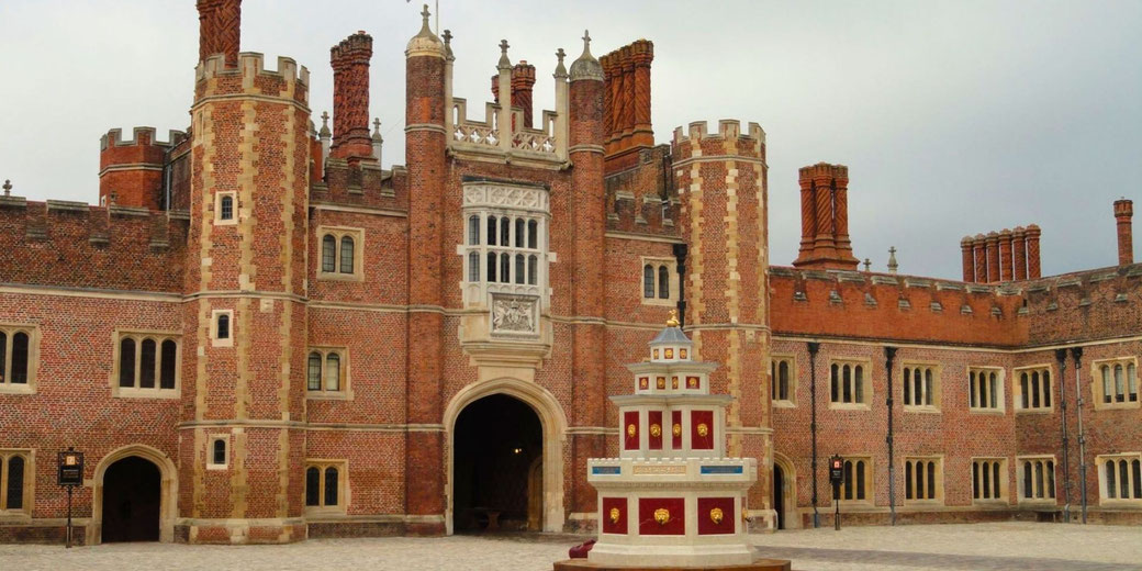Hampton Court Palace, a grand Tudor and Baroque palace in England, famously associated with Henry VIII. The red brick facade, ornate chimneys, and historic fountain highlight its royal heritage.