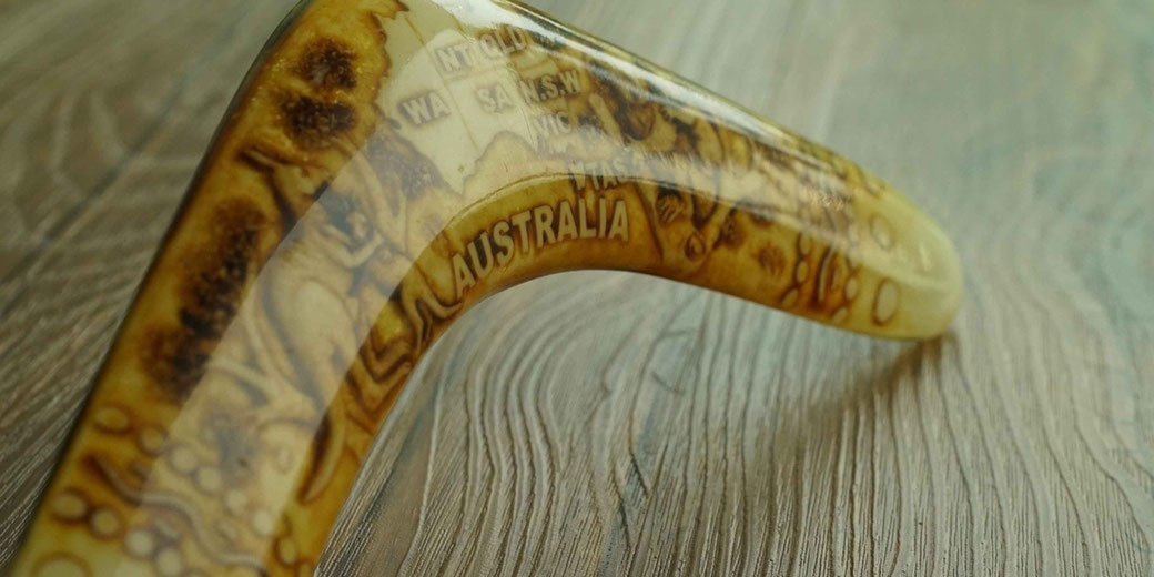 Boomerang with Aboriginal-style artwork and the word “Australia” displayed, photographed close up on a wooden surface with shallow depth of field.