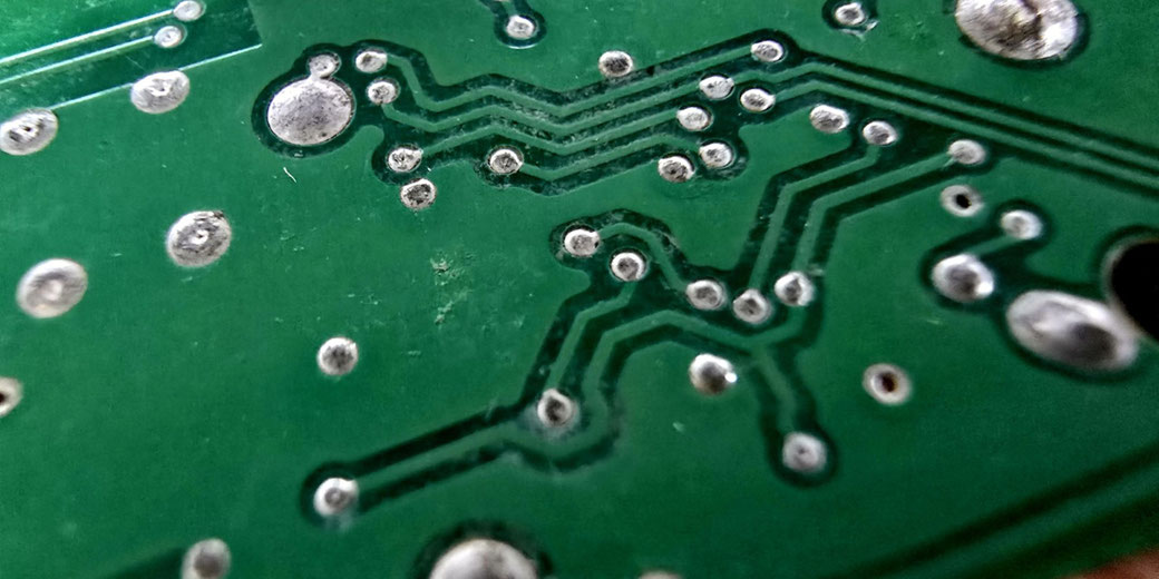 Close-up of a green printed circuit board showing metallic solder points and etched conductive pathways.