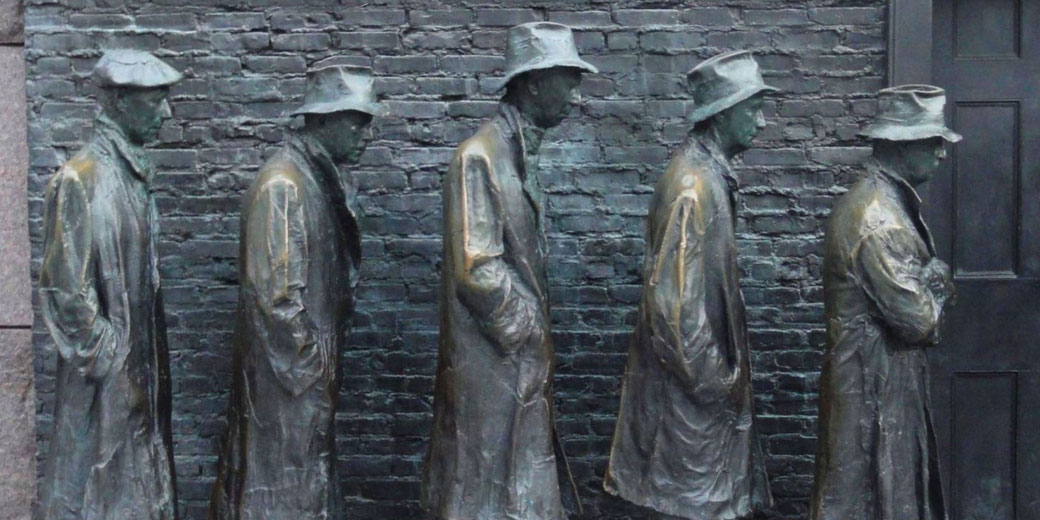 Bronze statues of men in coats and hats stand in a line against a brick wall, representing a breadline during the Great Depression.