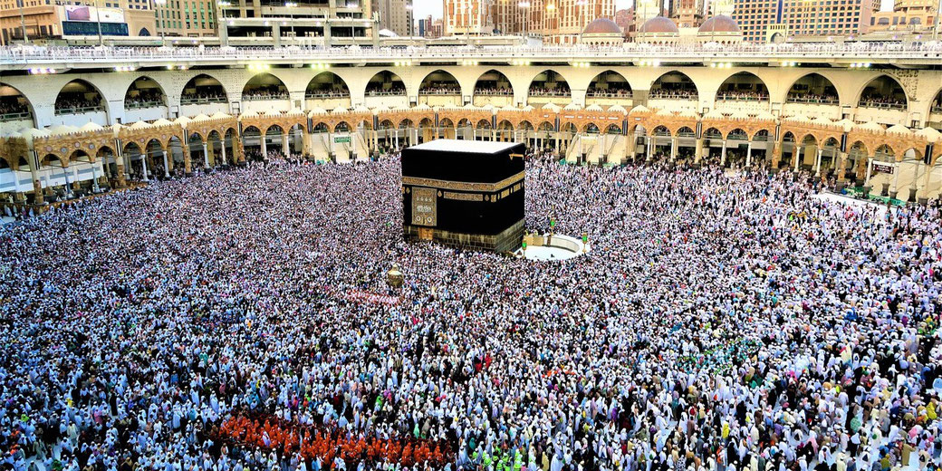 Massive crowd of pilgrims surrounds the Kaaba in Mecca during Hajj, all dressed in white garments, performing Tawaf in the Grand Mosque courtyard.