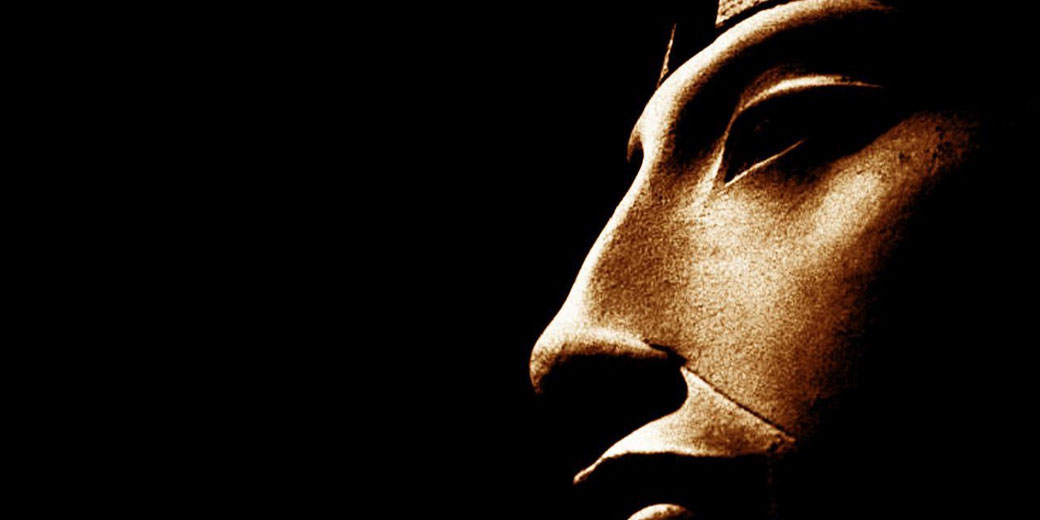 Close-up of an ancient Egyptian statue’s face in profile, dramatically lit against a black background.