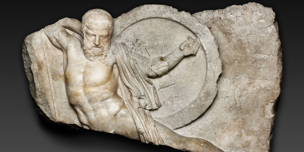 Ancient marble relief of a wounded warrior falling, with muscular detail, beard, shield, and tattered cloak, carved into a broken stone slab.