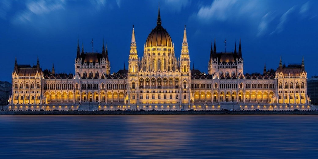 Illuminated Hungarian Parliament Building at night beside the Danube River, long exposure water and deep blue evening sky, symmetrical Gothic Revival architecture in Budapest.