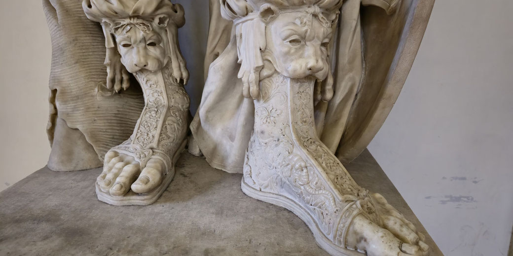 Close-up of marble sandals with intricate lion-head designs and ornate floral patterns, worn by a classical statue.