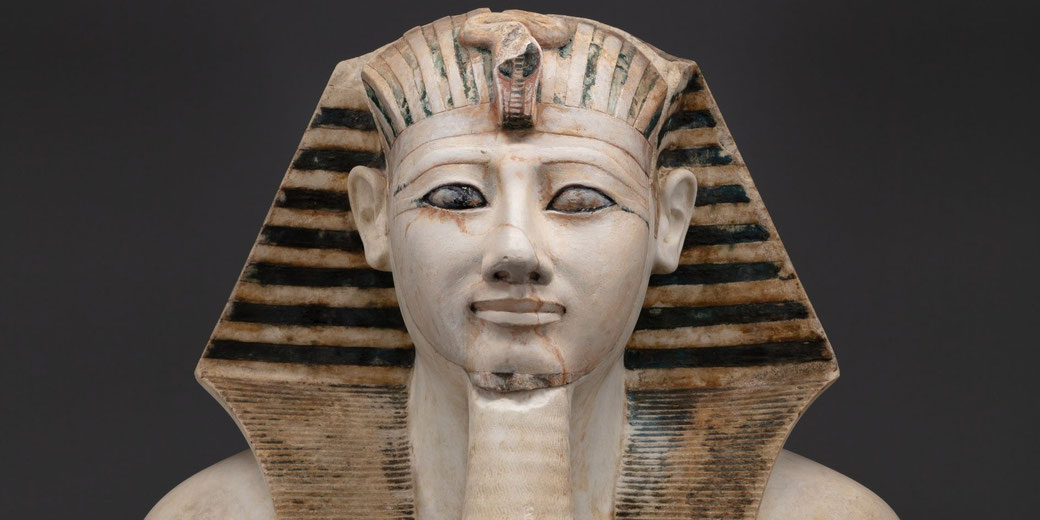 Carved limestone torso and head of Pharaoh Thutmose III, showing idealized royal features and muscular chest; originally part of a full statue from a temple at Deir el-Bahri.