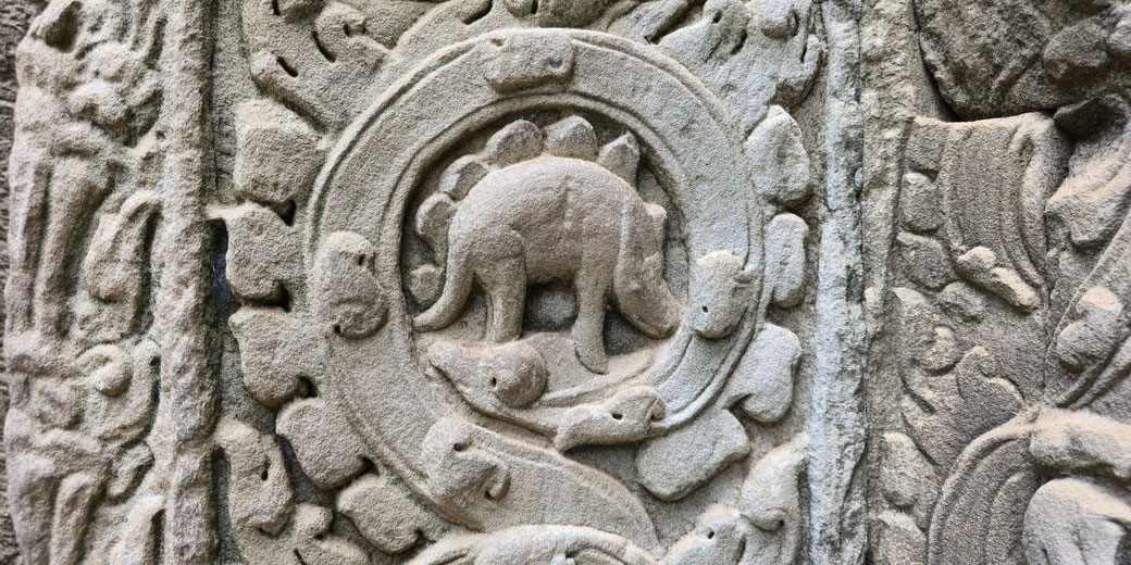 A stone carving features an animal with plates on its back, surrounded by decorative patterns in a circular frame.