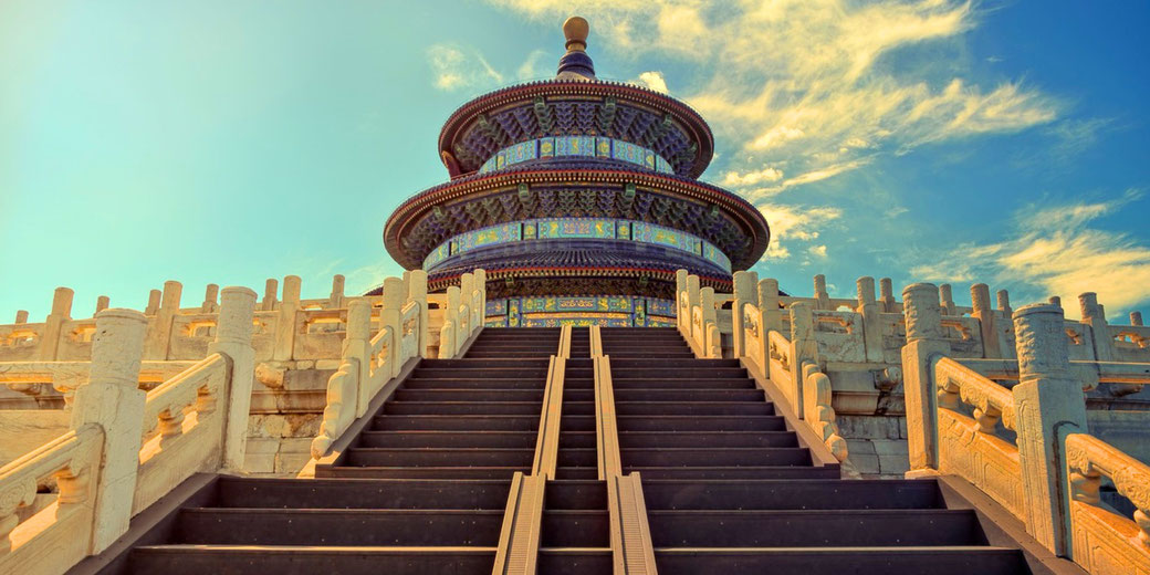 The Temple of Heaven in Beijing, China, with its ornate, circular design, intricate blue and gold details, and grand staircase leading up under a bright sky with scattered clouds.