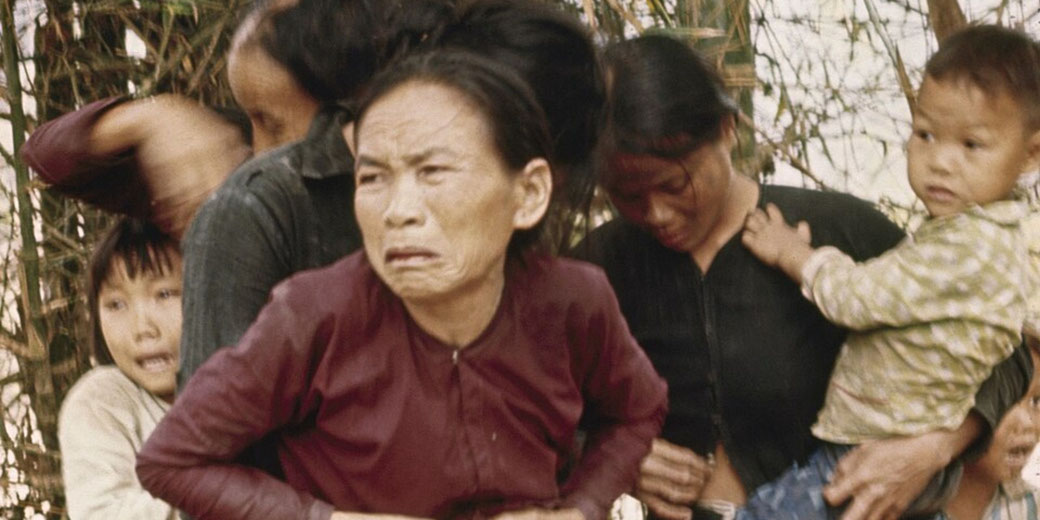 A distressed group of Vietnamese civilians, including women and children, react in fear during a moment of conflict or threat.