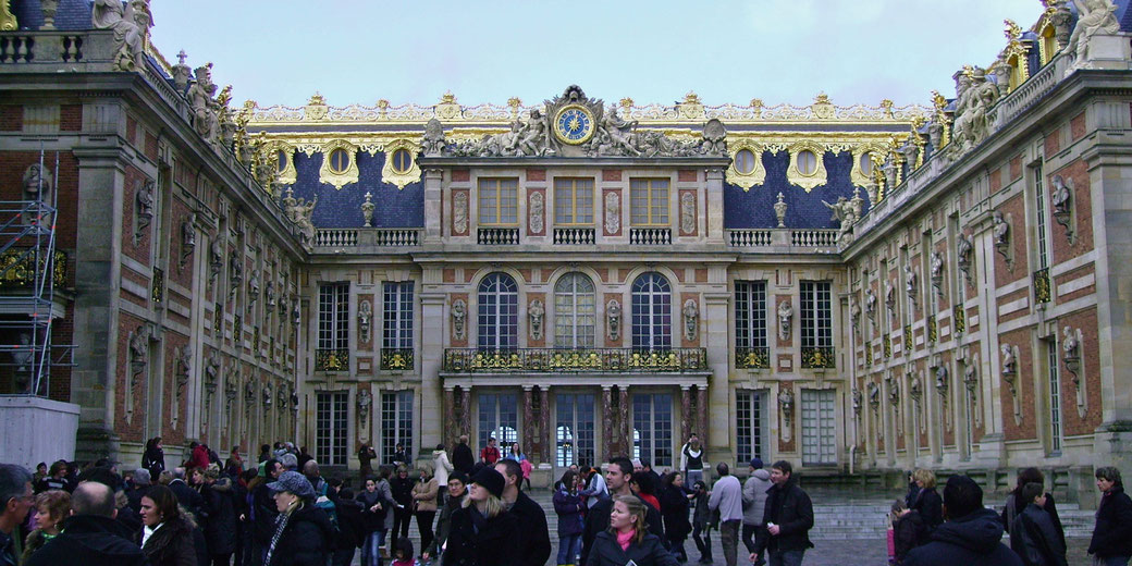 Crowd of visitors gathers in front of the lavishly decorated facade of the Palace of Versailles in France.