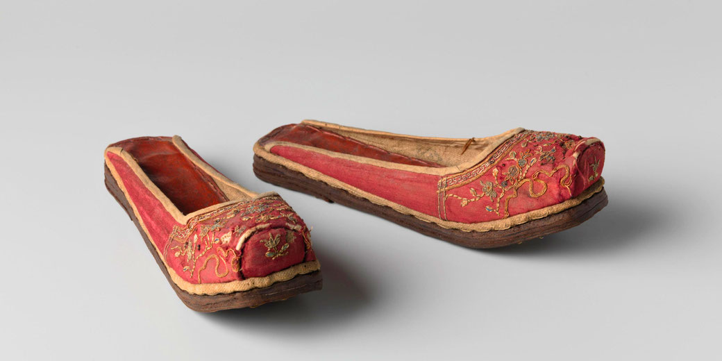 A pair of red embroidered Chinese slippers with intricate floral patterns and thick soles. These traditional shoes reflect historical craftsmanship and cultural elegance.