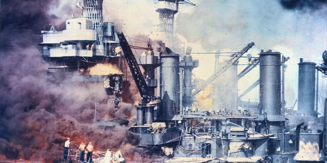 Warship engulfed in flames and thick smoke during battle, with crew on deck and industrial structures damaged amid explosions.