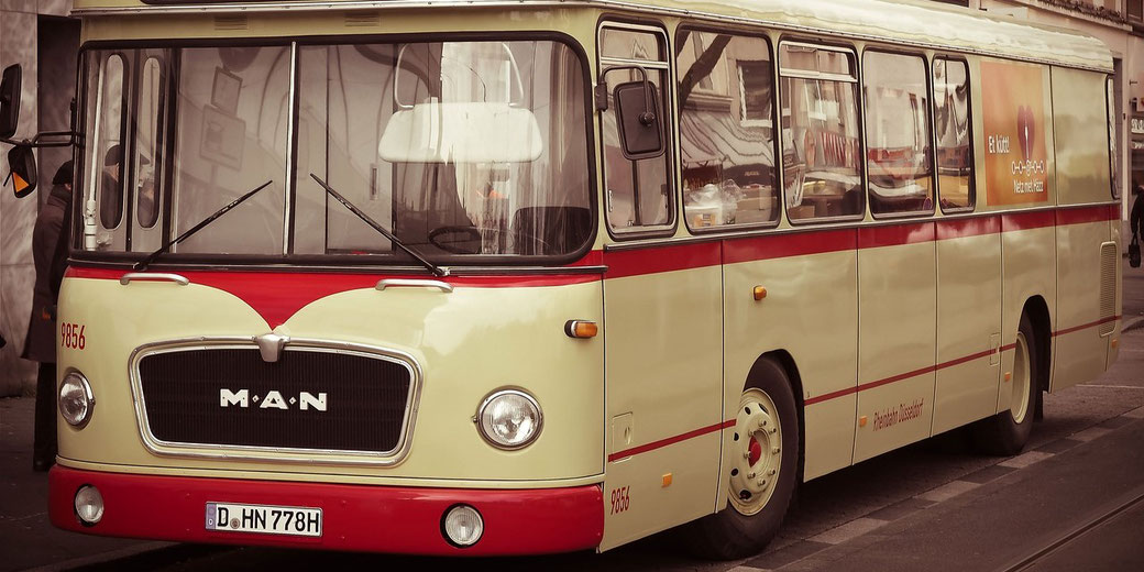 A vintage cream and red MAN bus is parked on a street, featuring rounded headlights and large windows.