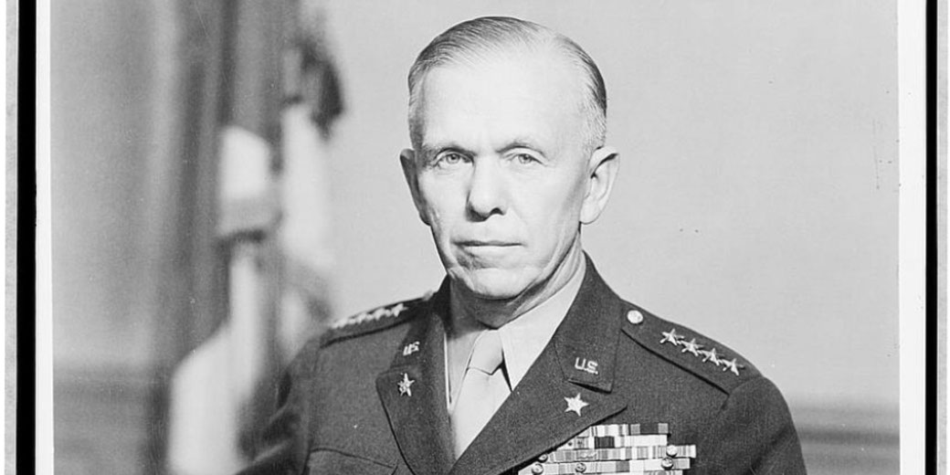 Black and white portrait of a senior U.S. Army general in formal uniform with medals and star insignia, facing the camera with a firm expression, blurred flag in the background.