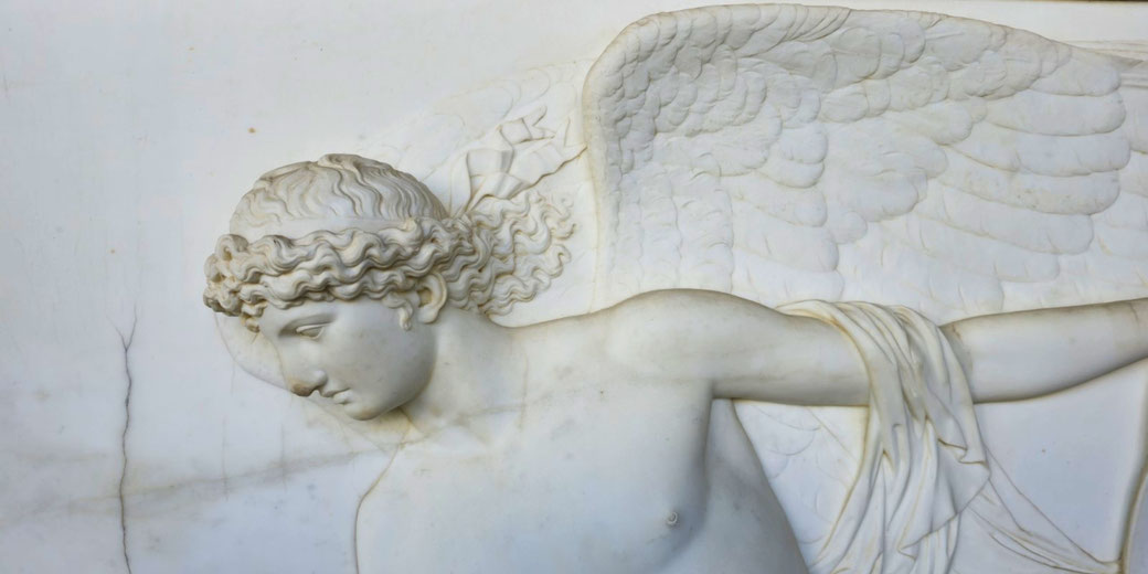 Marble relief of a winged figure with curly hair and a downward gaze, gracefully extending an arm draped in flowing fabric.