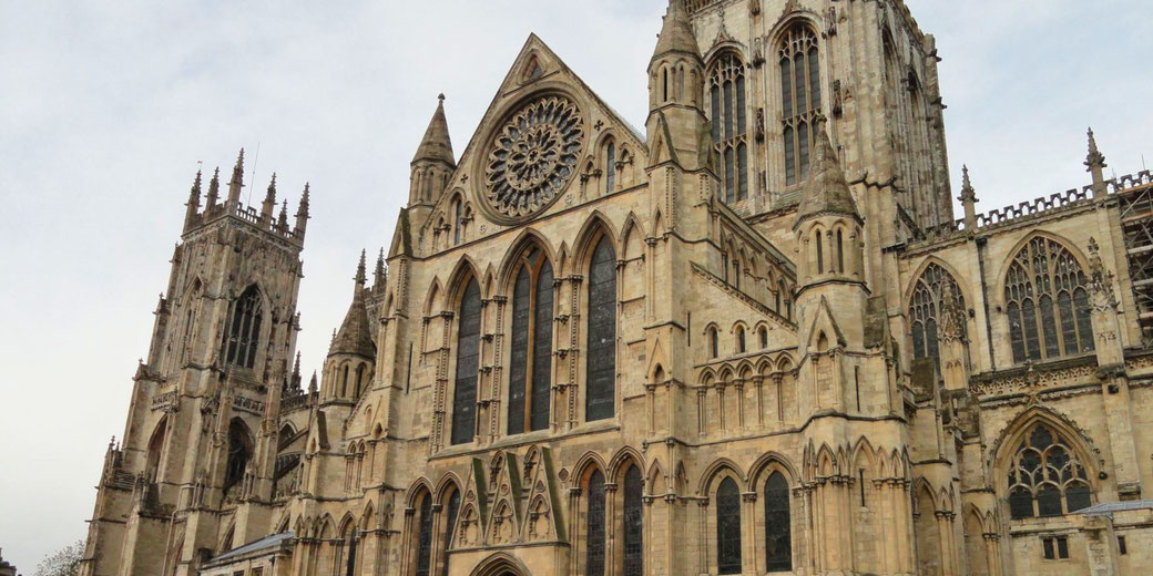 Gothic cathedral with pointed arches, tall towers, and a large rose window, set against a cloudy sky.
