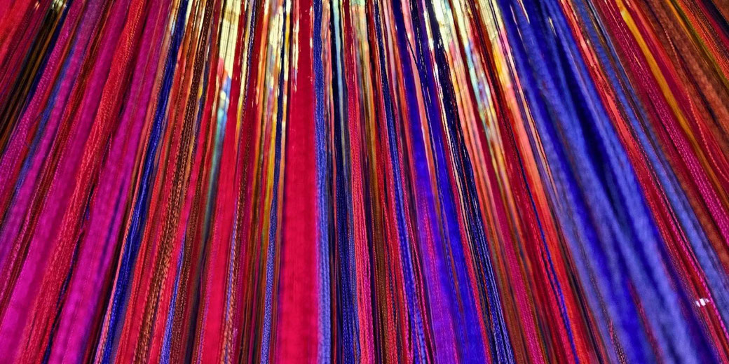 A vibrant close-up of multicolored threads hanging vertically, featuring rich shades of red, blue, and gold.