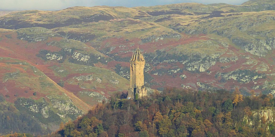The Wallace Monument, a towering sandstone structure atop Abbey Craig in Scotland, surrounded by rolling hills with autumn foliage, commemorating the legacy of William Wallace.